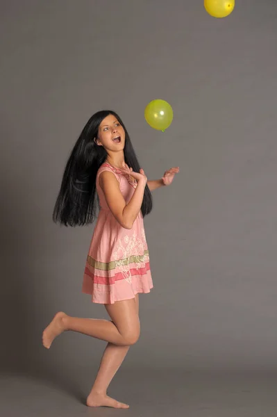 Brunette girl in a short pink dress with balloons plays on a gra — Stock Photo, Image