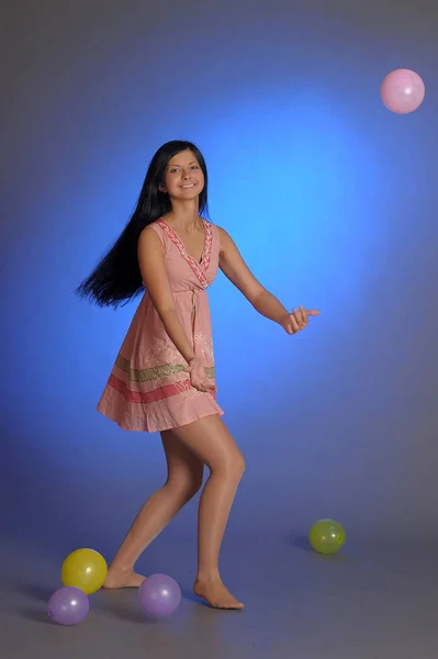 Брюнетка дівчина в короткій рожевій сукні з повітряними кулями грає на блакитному — стокове фото