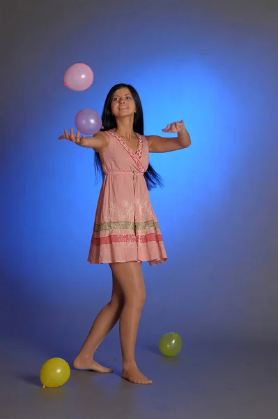 Brunette girl in a short pink dress with balloons plays on a blu — Stock Photo, Image