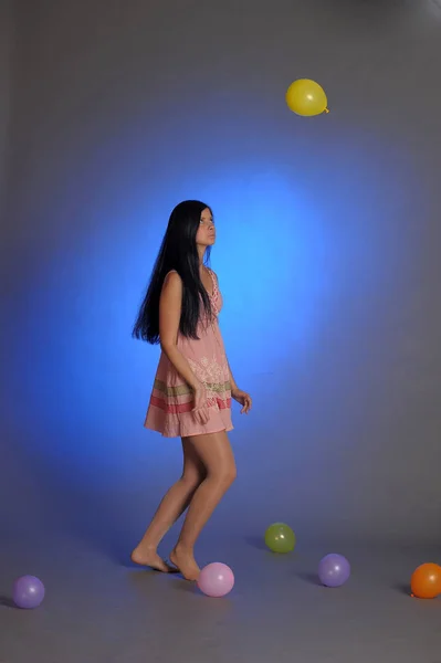 Brunette meisje in een korte roze jurk met ballonnen speelt op een blu — Stockfoto