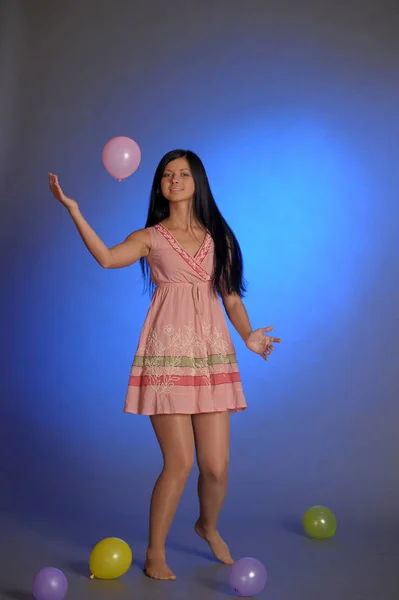 Brünettes Mädchen in einem kurzen rosa Kleid mit Luftballons spielt auf einem blu — Stockfoto