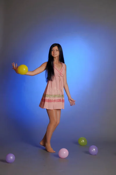 Menina morena em um vestido rosa curto com balões joga em um blu — Fotografia de Stock