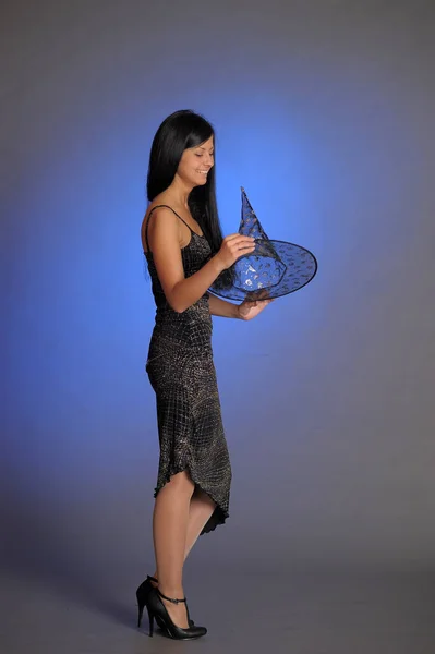 Brunett flicka i svart klänning och en häxa hatt på en blå bakgro — Stockfoto
