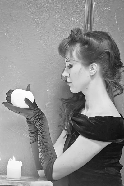 Brunette in een zwarte jurk en handschoenen met een kaars in haar handen — Stockfoto