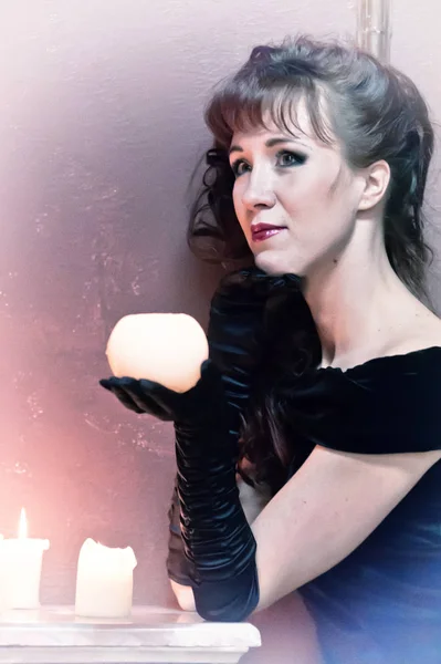 Brunette in a black dress and gloves with a candle in her hands — Stockfoto