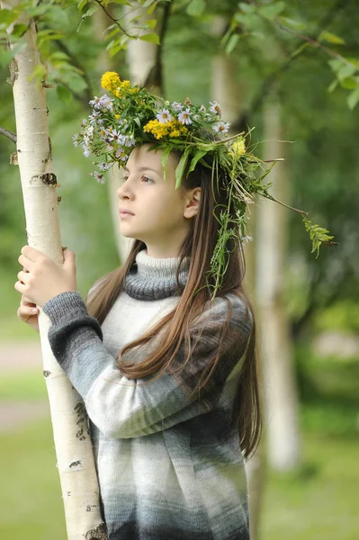 Mädchen mit einem Kranz aus Wildblumen auf dem Kopf nahe einer Birke — Stockfoto