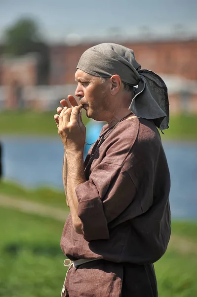A man in a medieval costume of a craftsman plays the pipe at the — Stock Photo, Image