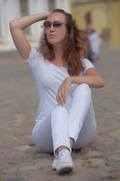 Woman in white trousers sits on the sidewalk in summer — 图库照片