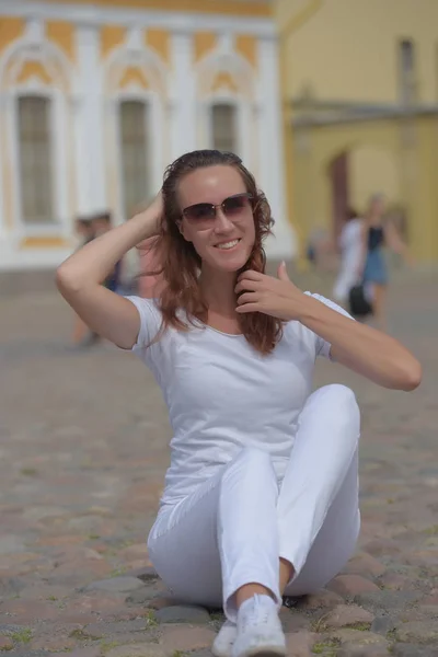 Женщина в белых брюках летом сидит на тротуаре — стоковое фото