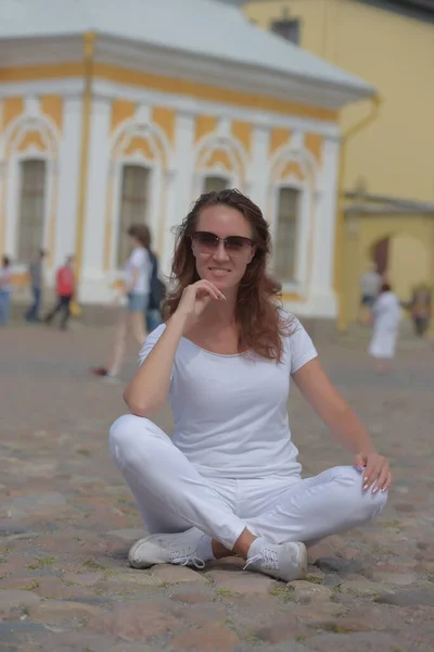 Woman in white trousers sits on the sidewalk in summer — Stok fotoğraf