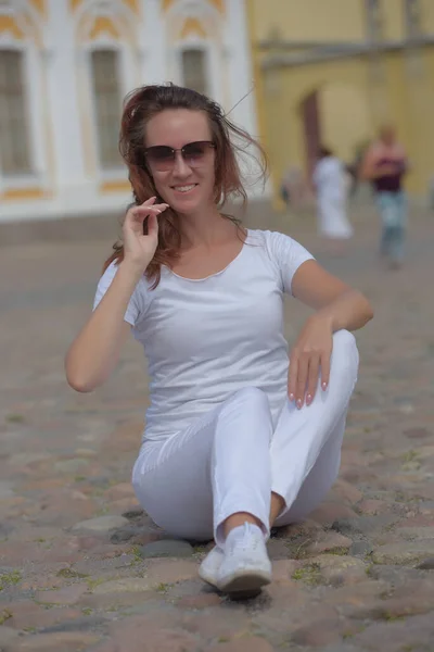 Woman in white trousers sits on the sidewalk in summer — Stok fotoğraf
