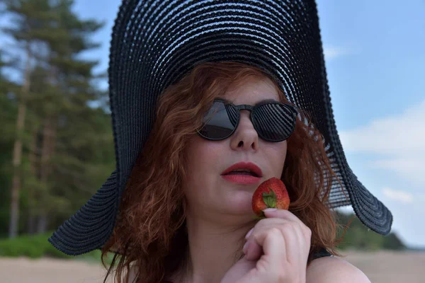Geniş Kenarlı Şapkalı Elinde Çilek Olan Güneş Gözlüklü Bir Kadının — Stok fotoğraf