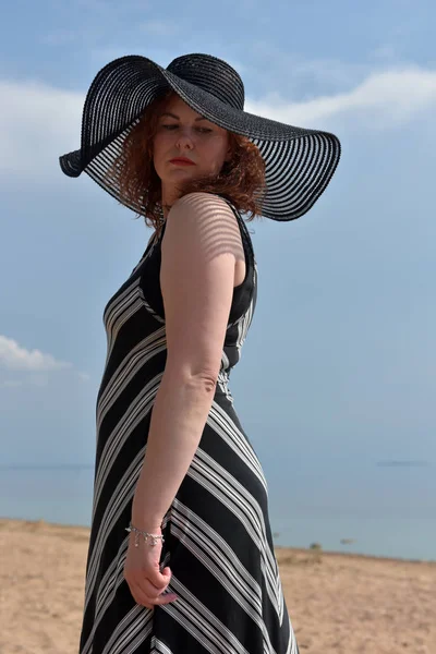 一个女人的肖像 戴着宽边帽 穿着条纹裙 背景在大海中 — 图库照片