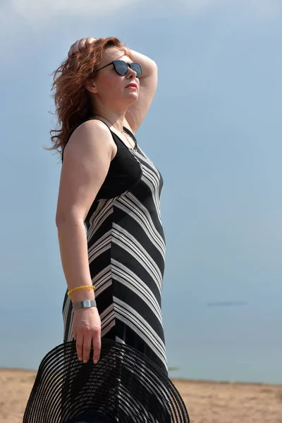 帽子を手に海を背景に縞模様のドレスを着た女性が — ストック写真