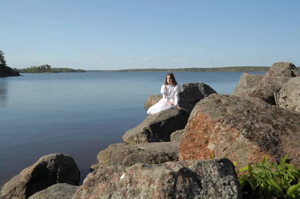 穿着白衣的小女孩坐在石头上的水边 — 图库照片