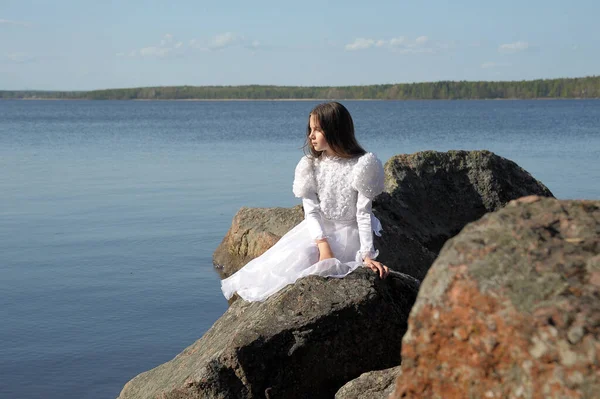 白いドレスを着た少女が石の上の水の近くに座り — ストック写真
