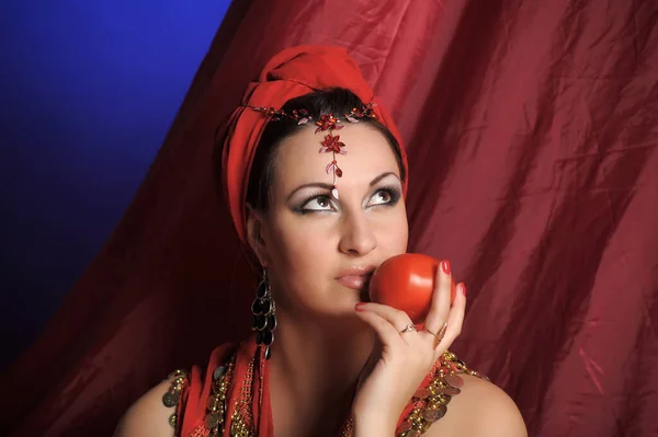 美しいですブルネット女性で赤東洋の服とともにターバンとジュエリー上の彼女の頭とスタジオで彼女の手の中にリンゴ — ストック写真