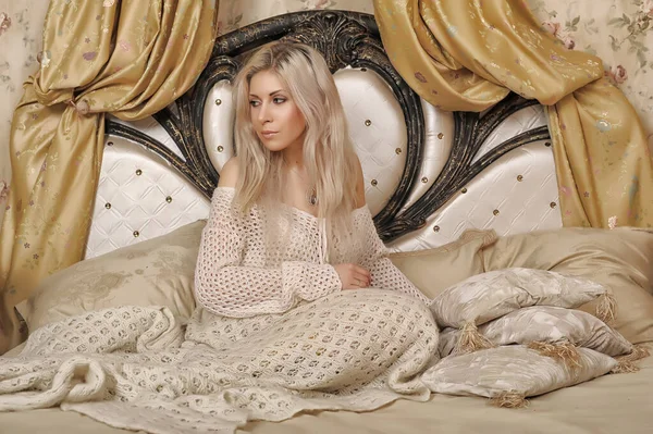 漂亮的金发姑娘 穿着一件白色针织毛衣坐在床上 裹着一件针织格子布 — 图库照片