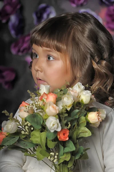 在演播室里 一个长着卷发 头戴白色毛衣 手上拿着花的黑发小女孩 她的背景是花的 — 图库照片