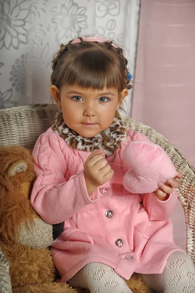 ピンクのセーターにおもちゃを着た女の子が椅子に座り — ストック写真