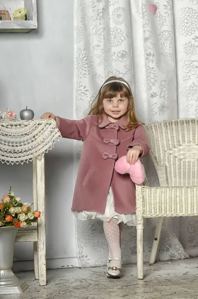一个穿着粉红外套的小女孩 穿着老式内饰的桌子旁边 — 图库照片