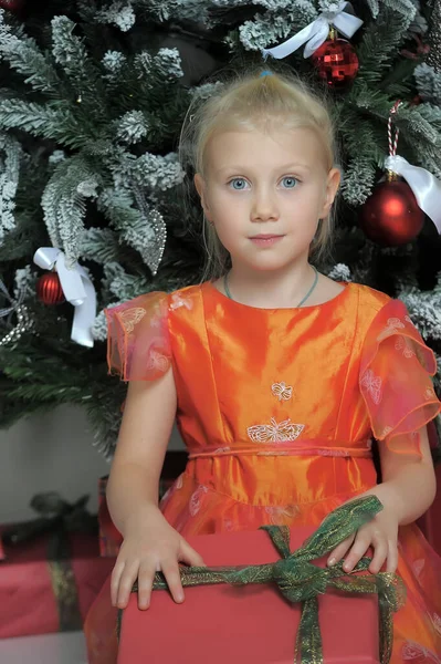 漂亮的金发小女孩穿着橙色的衣服 带着礼物 圣诞节的照片 — 图库照片
