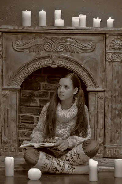 暖炉のそばの本とろうそくを持ったセーターの少女 — ストック写真