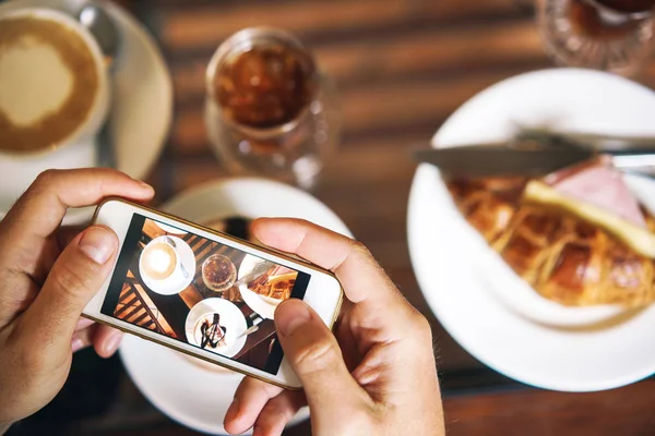 Hands with phone. Breakfast for two: a croissant with ham, coffee, a refreshing drink, sweetness.