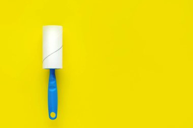 Silindir yapışkan bant ve sarı bir arka plan üzerindeki mavi kolu ile cleaner giyim. Düz yatıyordu arka plan.