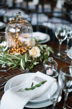 Düğün süslemeleri rustik tarzı ahşap bir masa üzerinde bir plaka üzerinde konuk kartı. Plaka, peçete, mumlar, karanfil ve çelenk.