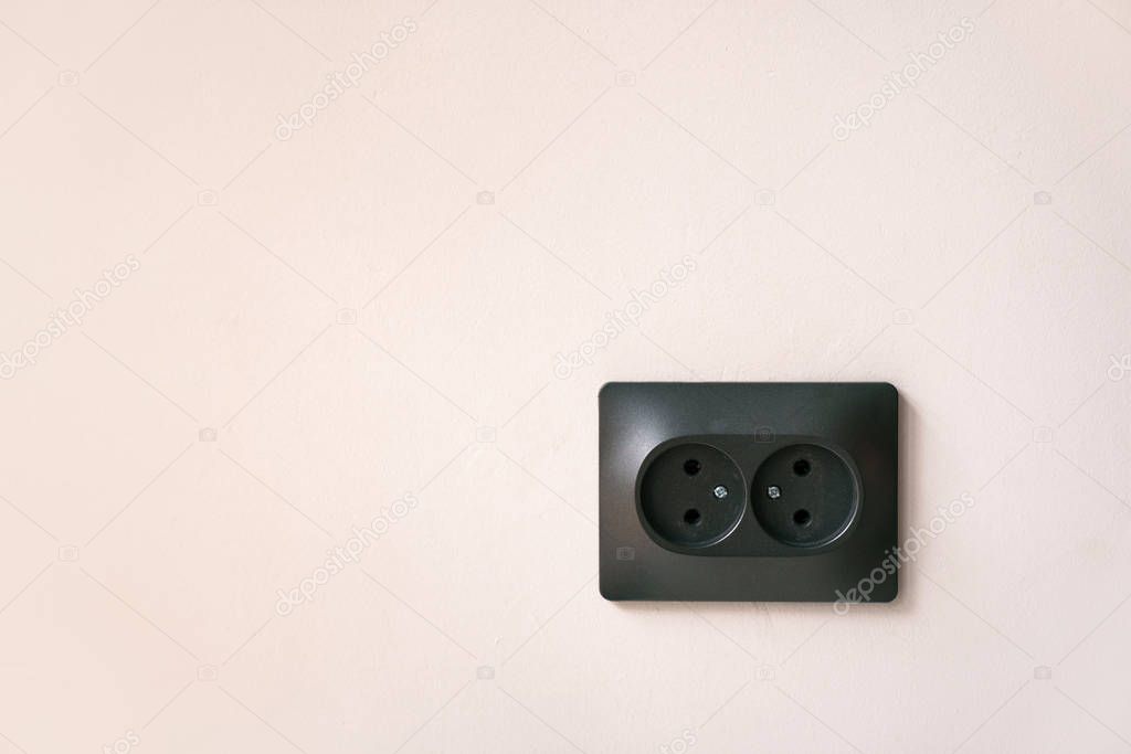black double electrical outlet on a light pink wall. Concept electricity and minimalism.