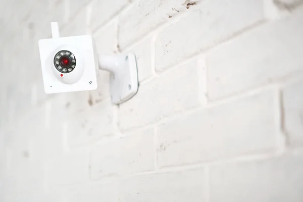 White web surveillance camera on a white brick wall. Security technologies.