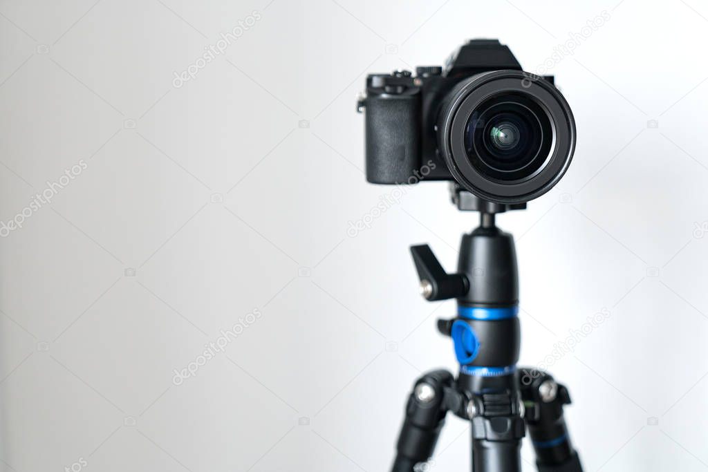 professional black mirrorless camera stands on a tripod against a white wall. Blogging and video photo shooting.