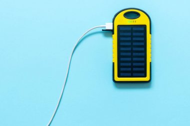 Mavi bir arka plan üzerinde sarı pil güneş enerjisi aygıt. Güneş panelinden akıllı telefon şarj.