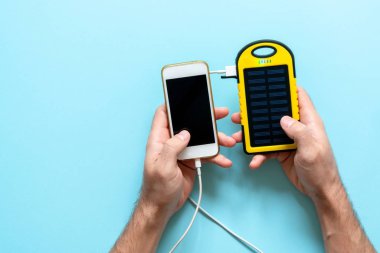 Sarı güneş enerjisi pil bir adam elinde mavi bir arka plan üzerinde bir cihazın. Güneş panelinden akıllı telefon şarj.