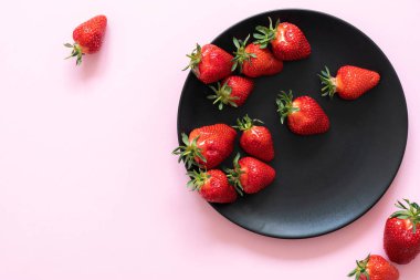 Pembe pastel bir arka plan siyah bir plaka üzerinde taze çilek pin-up. Kopya alanı.