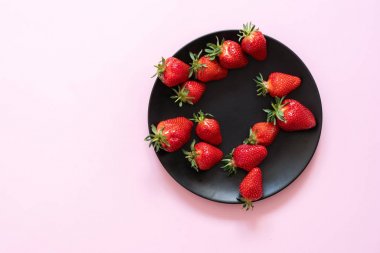 Pembe pastel bir arka plan siyah bir plaka üzerinde taze çilek pin-up. Uzay kopyalayın. Yukarıdan görüntülemek