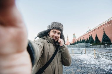 man takes a picture of himself against the backdrop of a red square in winter in Moscow, Russia. clipart