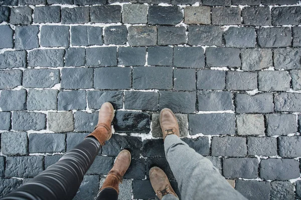 The legs of a man and a woman in leather shoes against the background of stone pavers laid out of stone. Travel together.