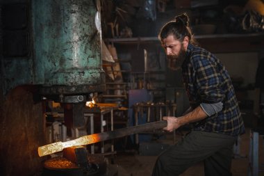Acımasız demirci atölyesini metal bir parça onun elinde tutan bir mekanik çekiç üzerinde çalışır. Bir meslek portresi.