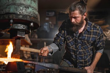 Çok acımasız Demirci Atölyesi mekanik çekiçle kızgın demir çalışır. Bir meslek portresi.