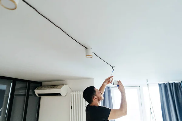 Man with a tool in his hands is repairing a lamp on the ceiling in his house. repair and improvement. — ストック写真