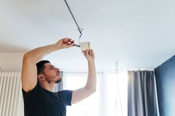 man with a screwdriver and pliers in his hands is engaged in repairing a lamp on the ceiling in his house. repair and improvement.