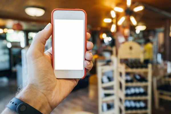 Макет смартфона в руке мужчины в красной рамке, на заднем плане магазин с теплым светом и полки с продуктами . — стоковое фото