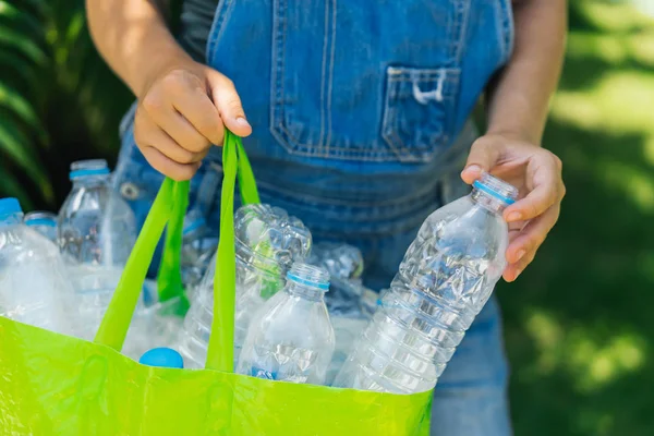 Пластиковая коллекция, охрана окружающей среды. Женские руки собирают бутылки и кладут в зеленый — стоковое фото