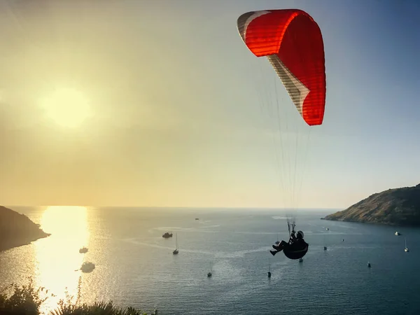 Bir adam yamaç paraşütü yapmakla meşgul. Mavi gökyüzünde yatın arka planında kırmızı paraşüt — Stok fotoğraf