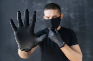 Siyah maskeli ve tıbbi eldivenli bir adam elinde siyah bir arka planda durduğunu gösteriyor. Coronavirus enfeksiyon koruma konsepti. COVID-19