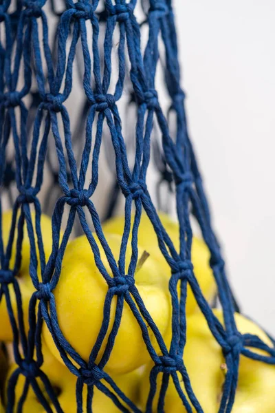 A string bag, a wicker bag made of blue rope with apples, stain plan, on a white background.