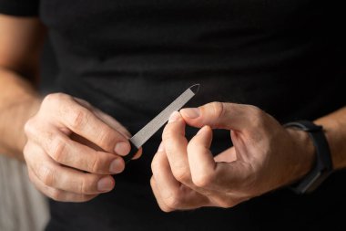 Karanlık bir arka planda erkek ellerini kapat. Bir adam çelik tırnak törpüsüyle manikür yapıyor..