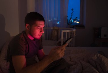 Evde yatakta yatan bir adam tabletten haber okur ya da film izler. Yatmadan önce evde akşam dersleri konsepti.